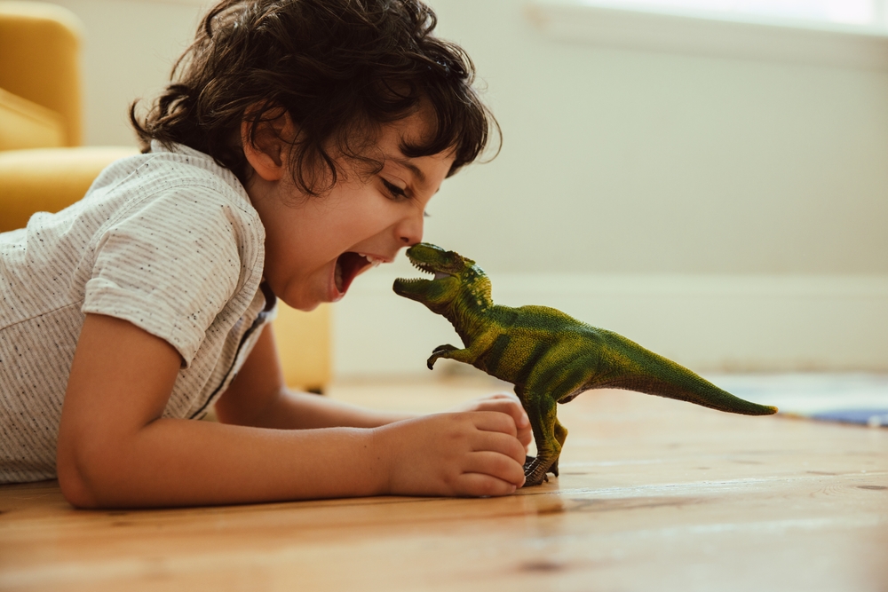 Adventurous,Young,Boy,Imitating,A,Dinosaur,Toy,While,Lying,On
